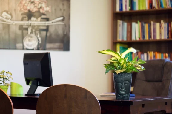 Ein moderner Arbeitsplatz mit Pflanzen, einem Computer und Bücherregal im Hintergrund.