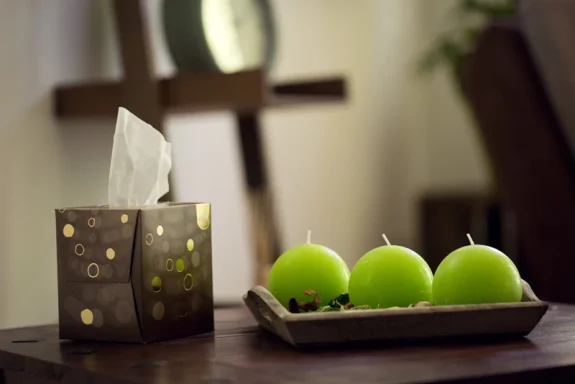 Grüne Kerzen und eine geprägte Papiertaschentuchbox auf einem Tisch.